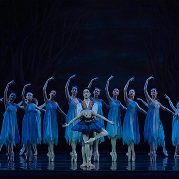 Ballerinas with right arm curved in the air, man and woman in center stage