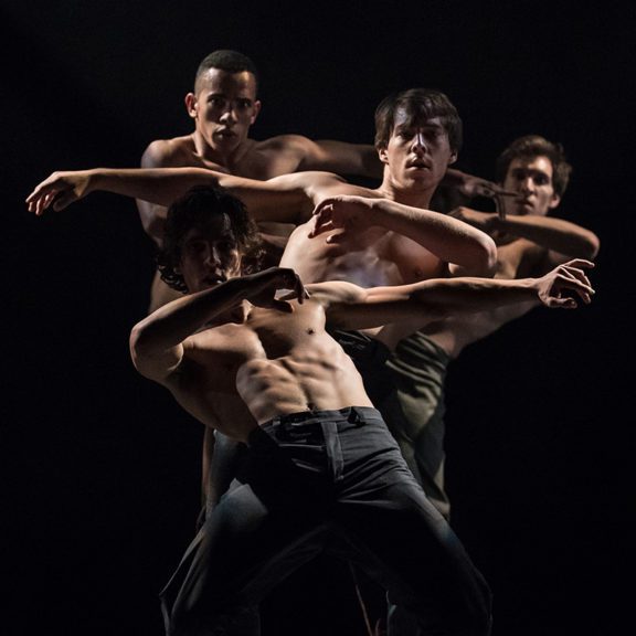 Four male dancers perform on stage
