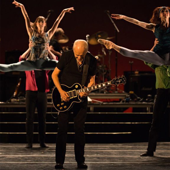 Man Playing Guitar On Stage With Ballet Dancers