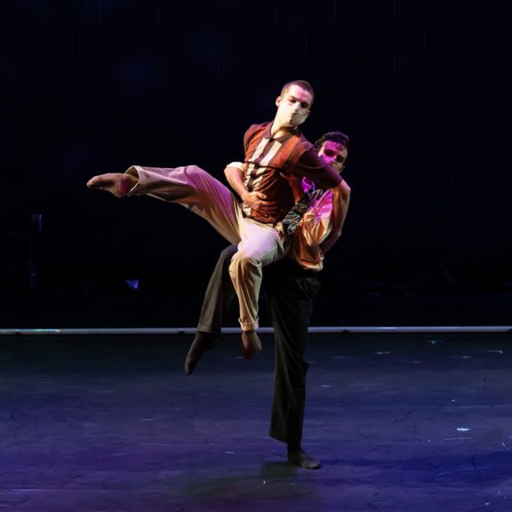 Two ballet dancers, one holding the other in the air on a stage