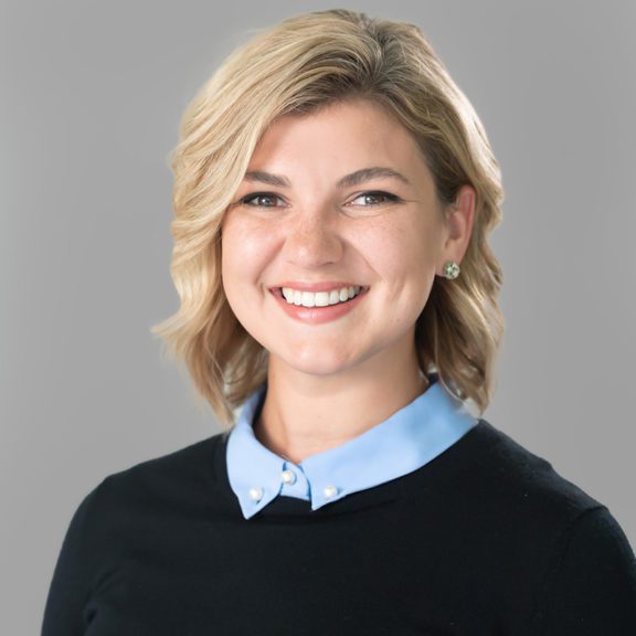 Photo of a woman with short blonde hair wearing a black sweater with a blue dress shirt