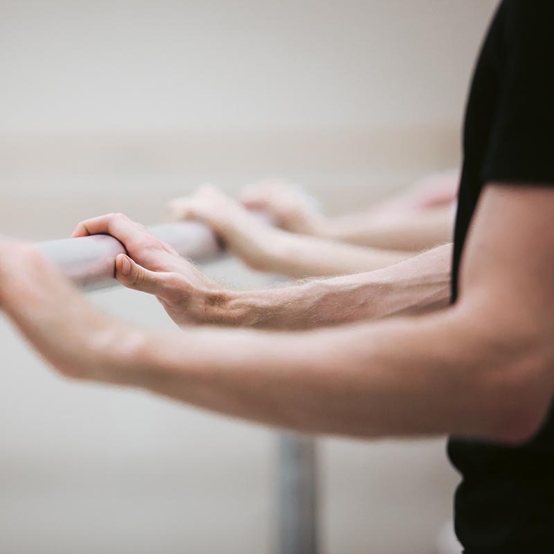 Photo of male ballet dancers' hands holding onto a metal ballet bar