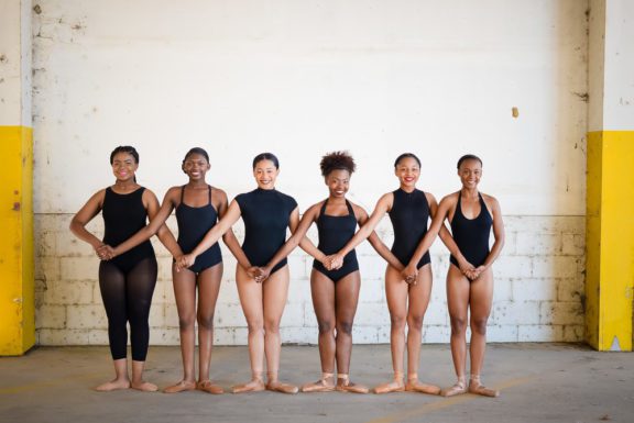 Photo of six female ballet dancers standing with their arms locked together