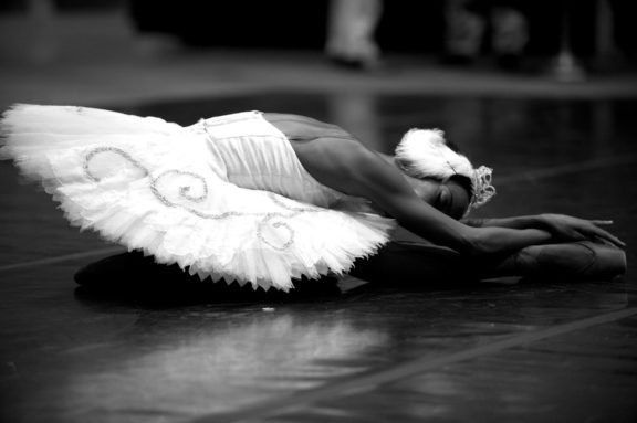 Black and white photo of a female ballet dancer bending down with her hands laying on her feet and her head laying on her leg