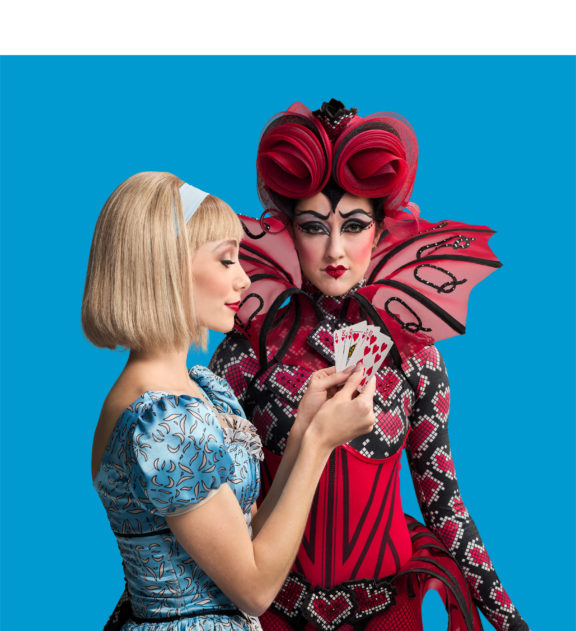 Photo of the Alice and Queen of Hearts characters from the Alice in Wonderland ballet performance posing for an image in front of a blue background