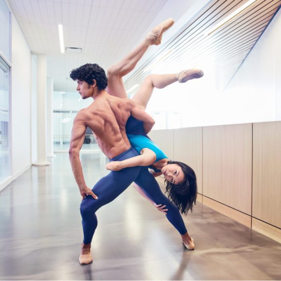 Photo of a shirtless male ballerina posed while holding a female ballerina around his body