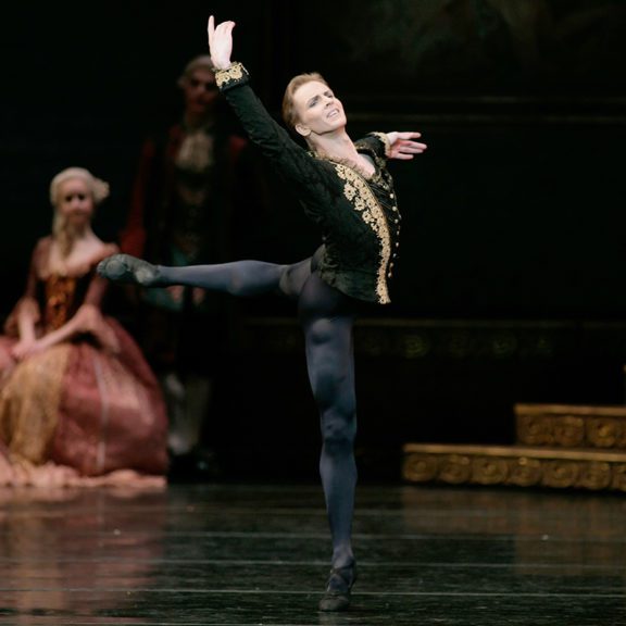 Photo of a male ballet dancer in a black costumer posing during a performance on stage