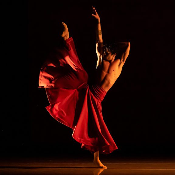 Photo of a male ballet dance wearing a red flowy costume on stage