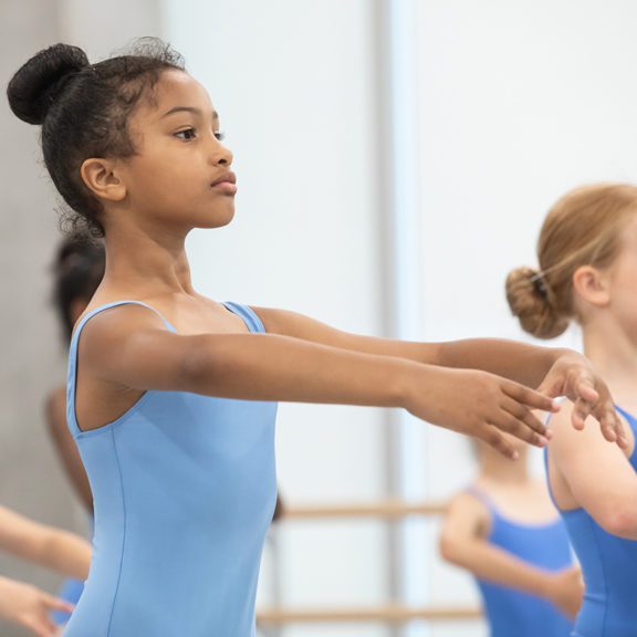 Photo of young female ballet dancers wearing blue leotards posing in a dance room